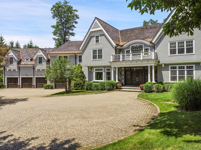 shingle-style home featuring decorative driveway, a balcony, and a front lawn