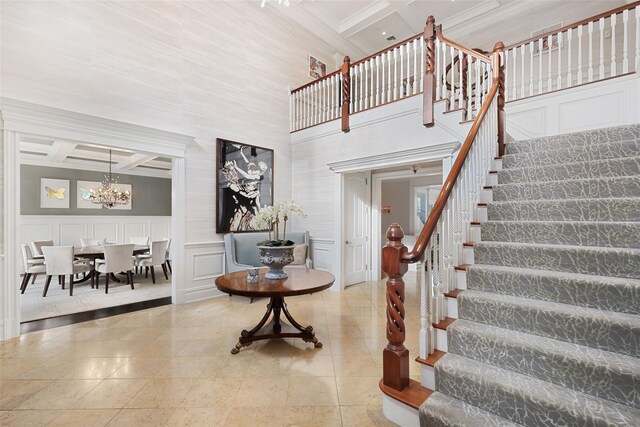 stairway featuring a wainscoted wall, beam ceiling, a notable chandelier, a decorative wall, and coffered ceiling