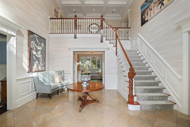 foyer entrance with beamed ceiling, ornamental molding, a towering ceiling, a decorative wall, and coffered ceiling