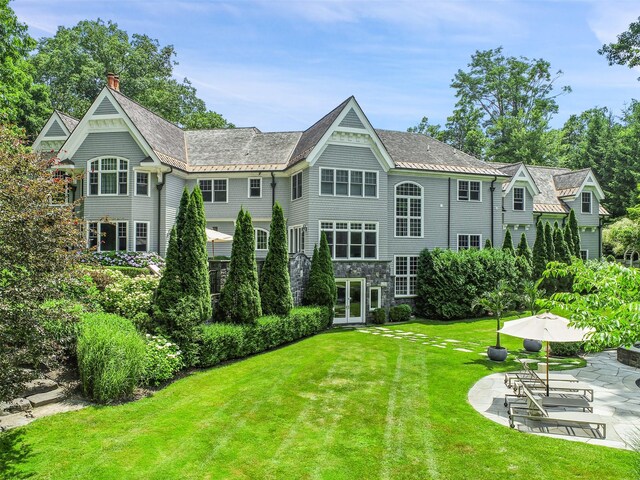 back of house with a chimney, french doors, stone siding, a patio area, and a lawn