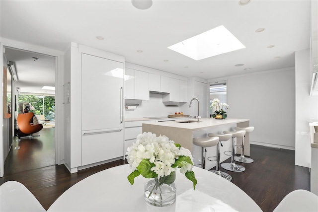 kitchen with sink, white cabinets, a skylight, dark hardwood / wood-style floors, and a kitchen island with sink