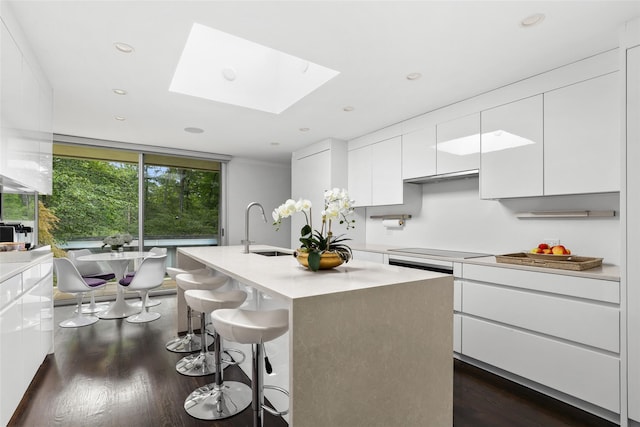 kitchen with sink, white cabinetry, a skylight, a kitchen island with sink, and dark wood-type flooring