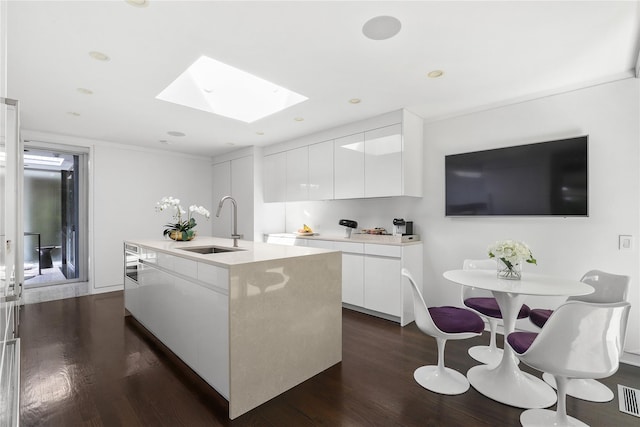 kitchen featuring a kitchen island with sink, a skylight, dark hardwood / wood-style flooring, white cabinetry, and sink