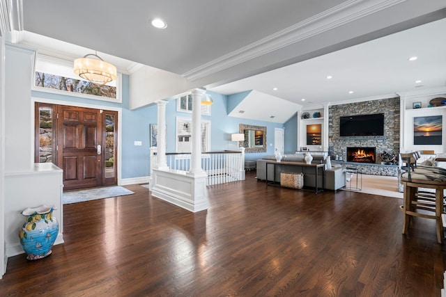 entrance foyer featuring dark wood-type flooring, lofted ceiling, a stone fireplace, ornamental molding, and decorative columns