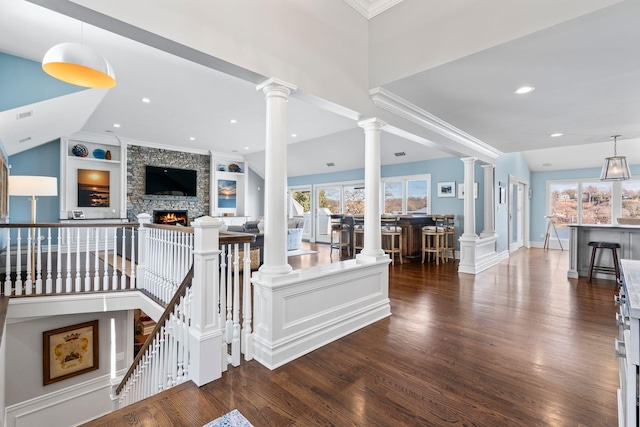 interior space featuring a stone fireplace, crown molding, built in features, hardwood / wood-style flooring, and decorative columns