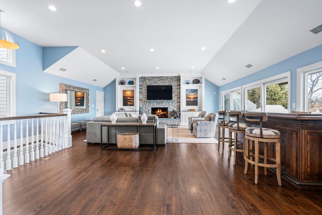 living room with lofted ceiling, a stone fireplace, dark hardwood / wood-style flooring, and built in shelves