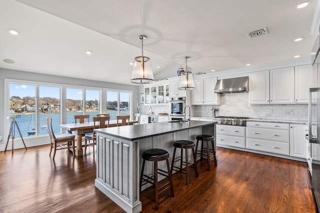 kitchen featuring white cabinetry, an island with sink, a water view, and wall chimney exhaust hood