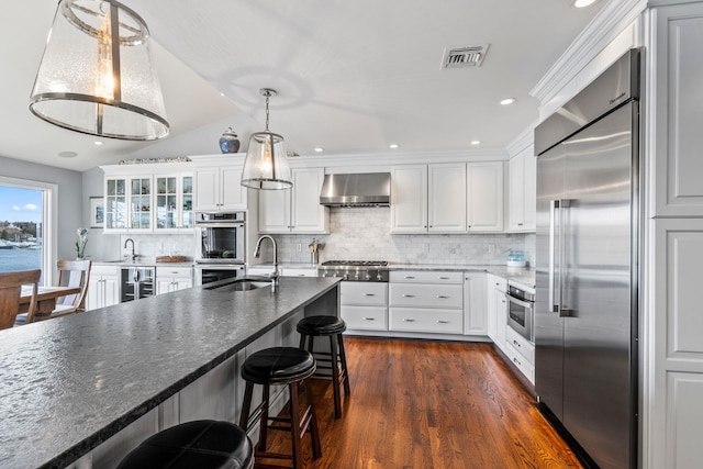 kitchen with white cabinetry, stainless steel appliances, sink, and wall chimney range hood