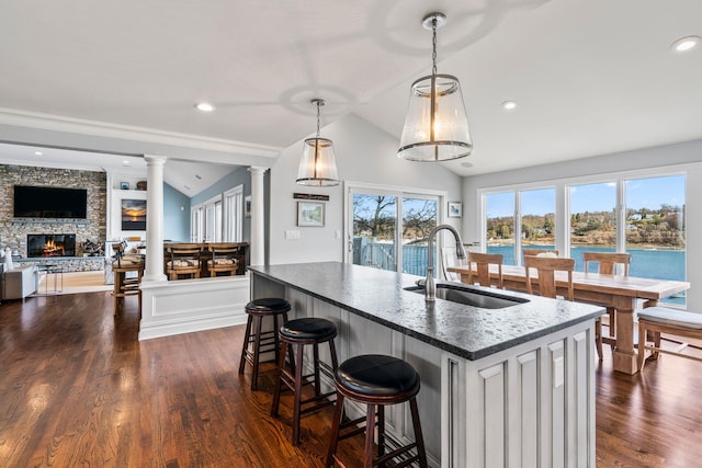 kitchen featuring sink, a water view, decorative light fixtures, vaulted ceiling, and decorative columns