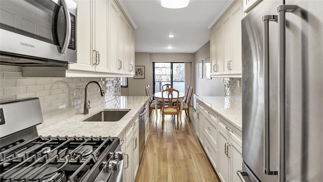 kitchen featuring stainless steel appliances, tasteful backsplash, sink, light wood-type flooring, and light stone counters