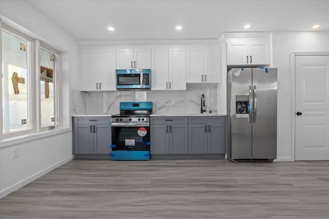 kitchen with backsplash, gray cabinetry, stainless steel appliances, light hardwood / wood-style flooring, and white cabinets