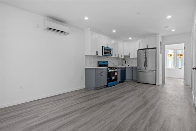 kitchen featuring a wall mounted air conditioner, white cabinets, appliances with stainless steel finishes, and light hardwood / wood-style flooring