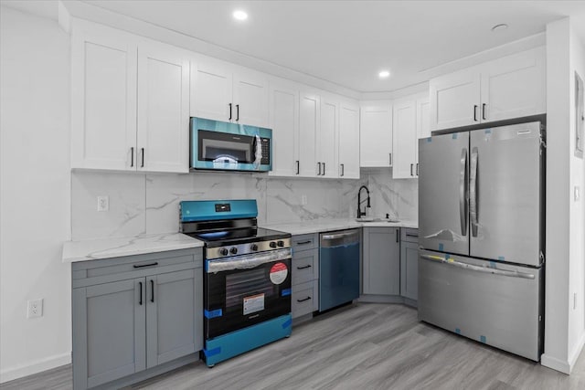 kitchen featuring white cabinetry, sink, light hardwood / wood-style flooring, decorative backsplash, and appliances with stainless steel finishes