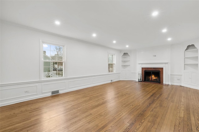 unfurnished living room featuring a fireplace, crown molding, built in features, and hardwood / wood-style floors