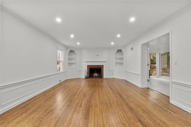 unfurnished living room featuring built in features, ornamental molding, light hardwood / wood-style floors, and a brick fireplace