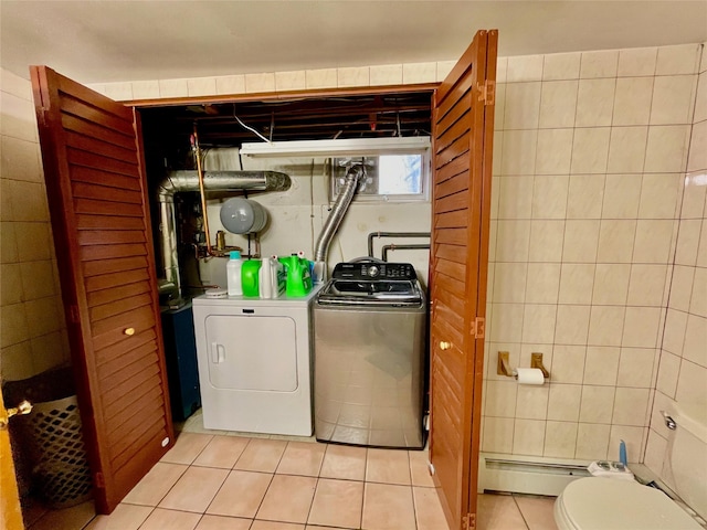 laundry room featuring washing machine and dryer, light tile patterned floors, tile walls, and a baseboard heating unit