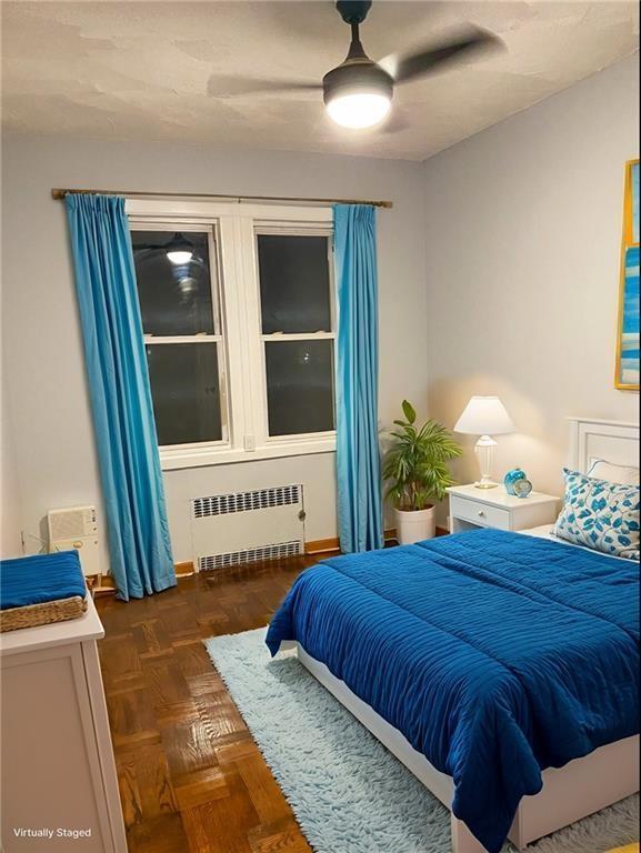 bedroom with dark parquet flooring, ceiling fan, and radiator heating unit