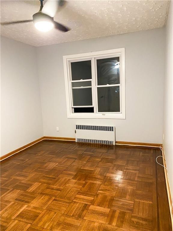 unfurnished room featuring dark parquet floors, ceiling fan, radiator heating unit, and a textured ceiling