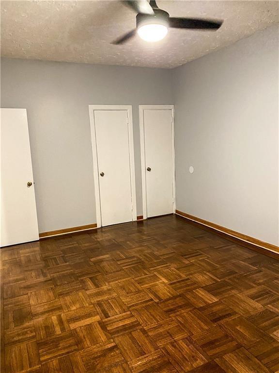 unfurnished bedroom with dark parquet floors, ceiling fan, and a textured ceiling