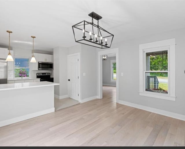 kitchen featuring decorative light fixtures, stainless steel appliances, an inviting chandelier, light wood-type flooring, and white cabinetry