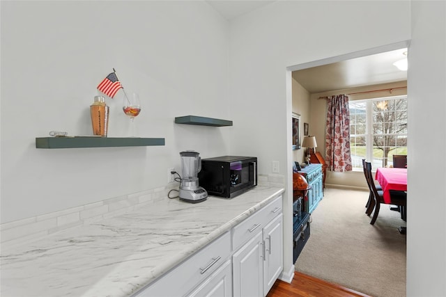 kitchen featuring white cabinets, light stone counters, and light carpet