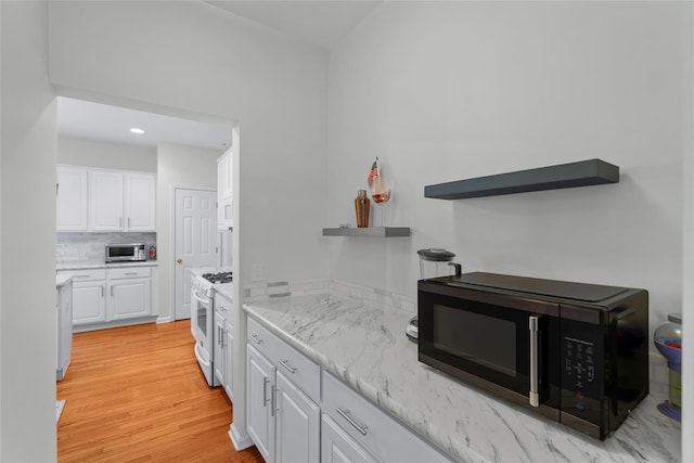 kitchen featuring white cabinetry, white gas range oven, light stone counters, light hardwood / wood-style flooring, and tasteful backsplash