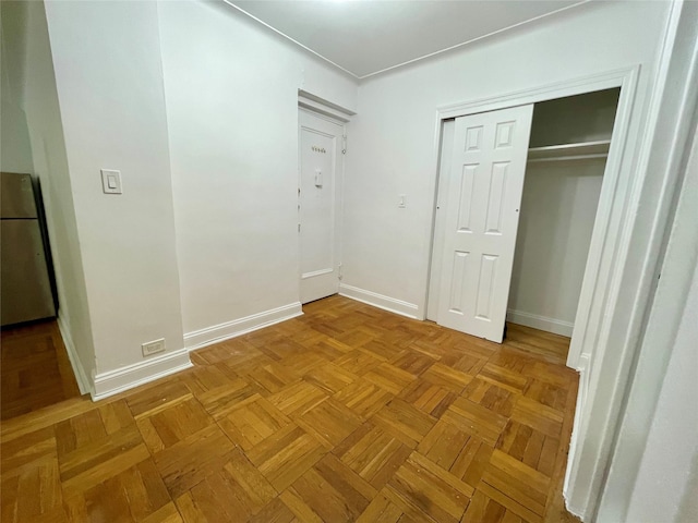 unfurnished bedroom featuring a closet, stainless steel refrigerator, and light parquet flooring