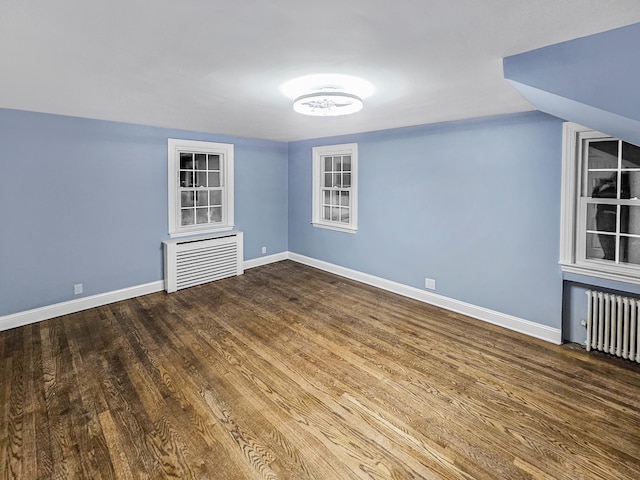 empty room featuring radiator heating unit, vaulted ceiling, and hardwood / wood-style flooring