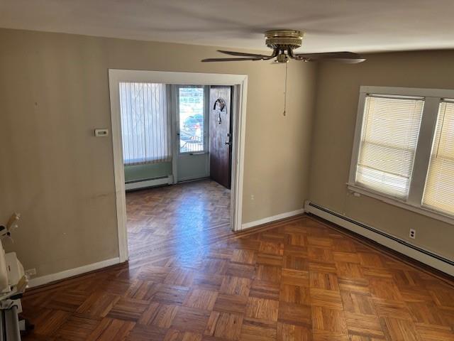 interior space with dark parquet floors, ceiling fan, and a baseboard heating unit