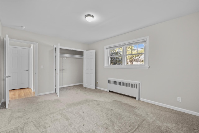 unfurnished bedroom with radiator heating unit, light colored carpet, and a closet