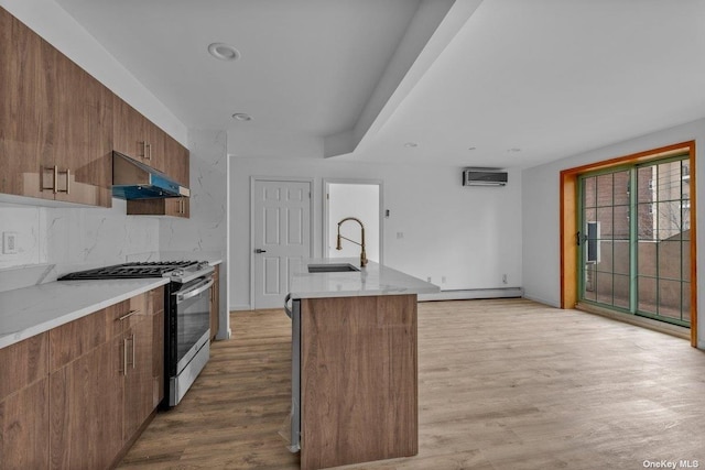 kitchen featuring stainless steel gas range oven, an AC wall unit, sink, light wood-type flooring, and baseboard heating