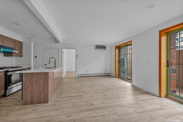 kitchen with a breakfast bar, baseboard heating, a kitchen island with sink, sink, and stainless steel range with gas cooktop