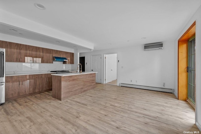 kitchen featuring a center island with sink, light hardwood / wood-style flooring, baseboard heating, tasteful backsplash, and extractor fan