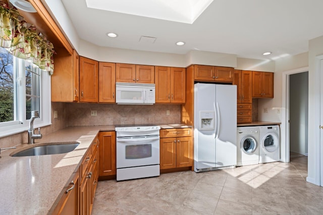 kitchen with sink, washing machine and clothes dryer, light stone counters, white appliances, and tasteful backsplash