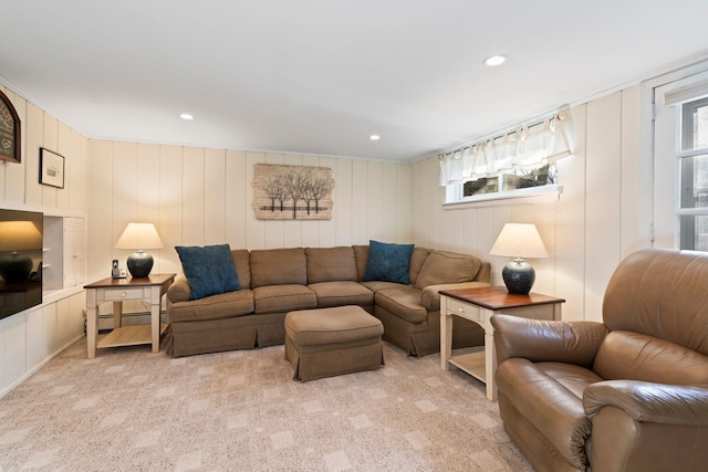 living room featuring wooden walls, a baseboard heating unit, plenty of natural light, and light colored carpet