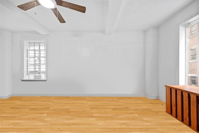 empty room with beamed ceiling, light hardwood / wood-style flooring, and a healthy amount of sunlight