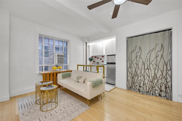 sitting room featuring a ceiling fan, light wood-style flooring, baseboards, and beamed ceiling