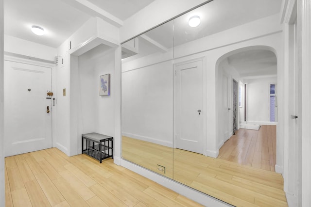 hallway featuring baseboards, wood finished floors, and arched walkways