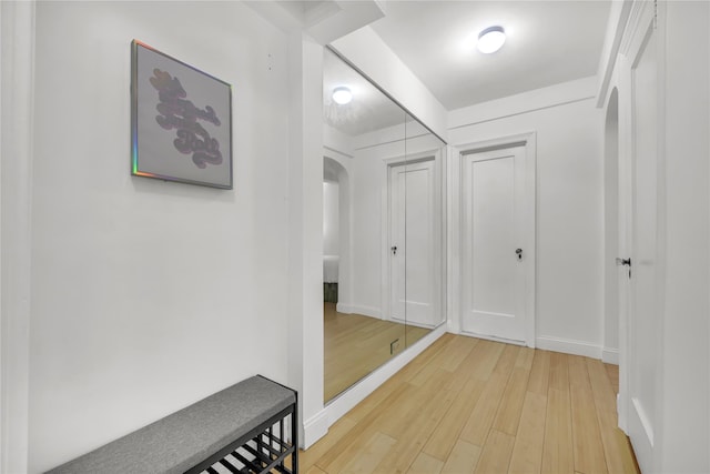 corridor featuring baseboards, arched walkways, and light wood-style flooring