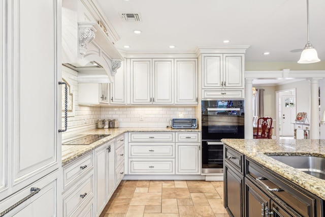 kitchen with light stone countertops, custom range hood, black appliances, white cabinetry, and hanging light fixtures