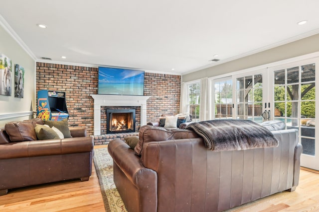 living room featuring french doors, a brick fireplace, light hardwood / wood-style flooring, brick wall, and ornamental molding