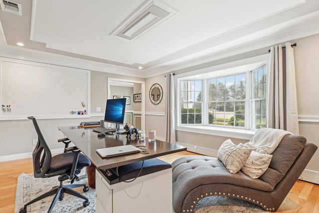 home office with light hardwood / wood-style floors, a raised ceiling, and crown molding