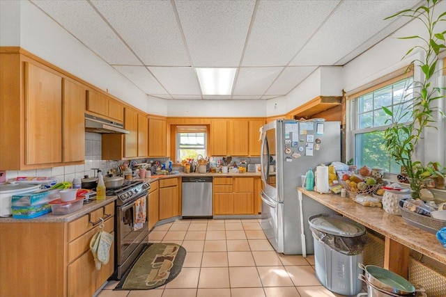 kitchen featuring a paneled ceiling, appliances with stainless steel finishes, decorative backsplash, and light tile patterned floors