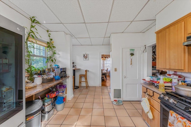 kitchen featuring gas stove, light tile patterned floors, a drop ceiling, and refrigerator