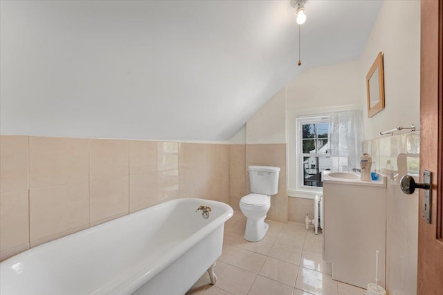 bathroom featuring lofted ceiling, tile walls, a tub to relax in, tile patterned flooring, and toilet