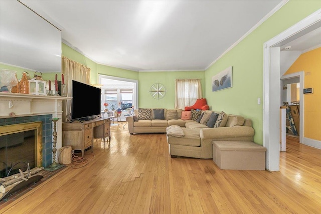 living room featuring a tile fireplace, crown molding, and light wood-type flooring