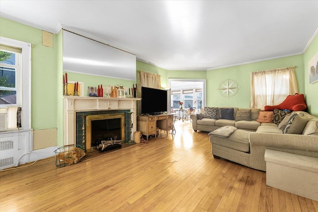 living room featuring a tile fireplace, crown molding, and light hardwood / wood-style floors