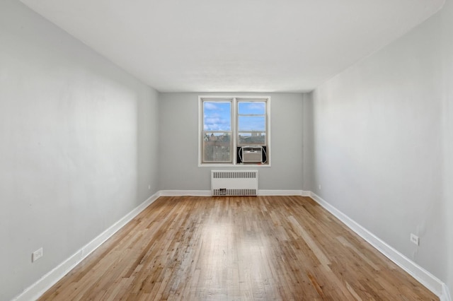 empty room featuring cooling unit, radiator heating unit, and light hardwood / wood-style flooring