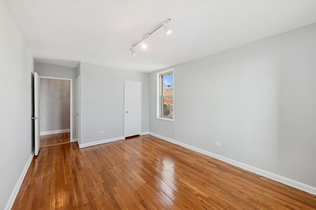 unfurnished bedroom with hardwood / wood-style floors and rail lighting