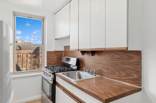 kitchen featuring stainless steel gas stove, white refrigerator, white cabinetry, and a wealth of natural light